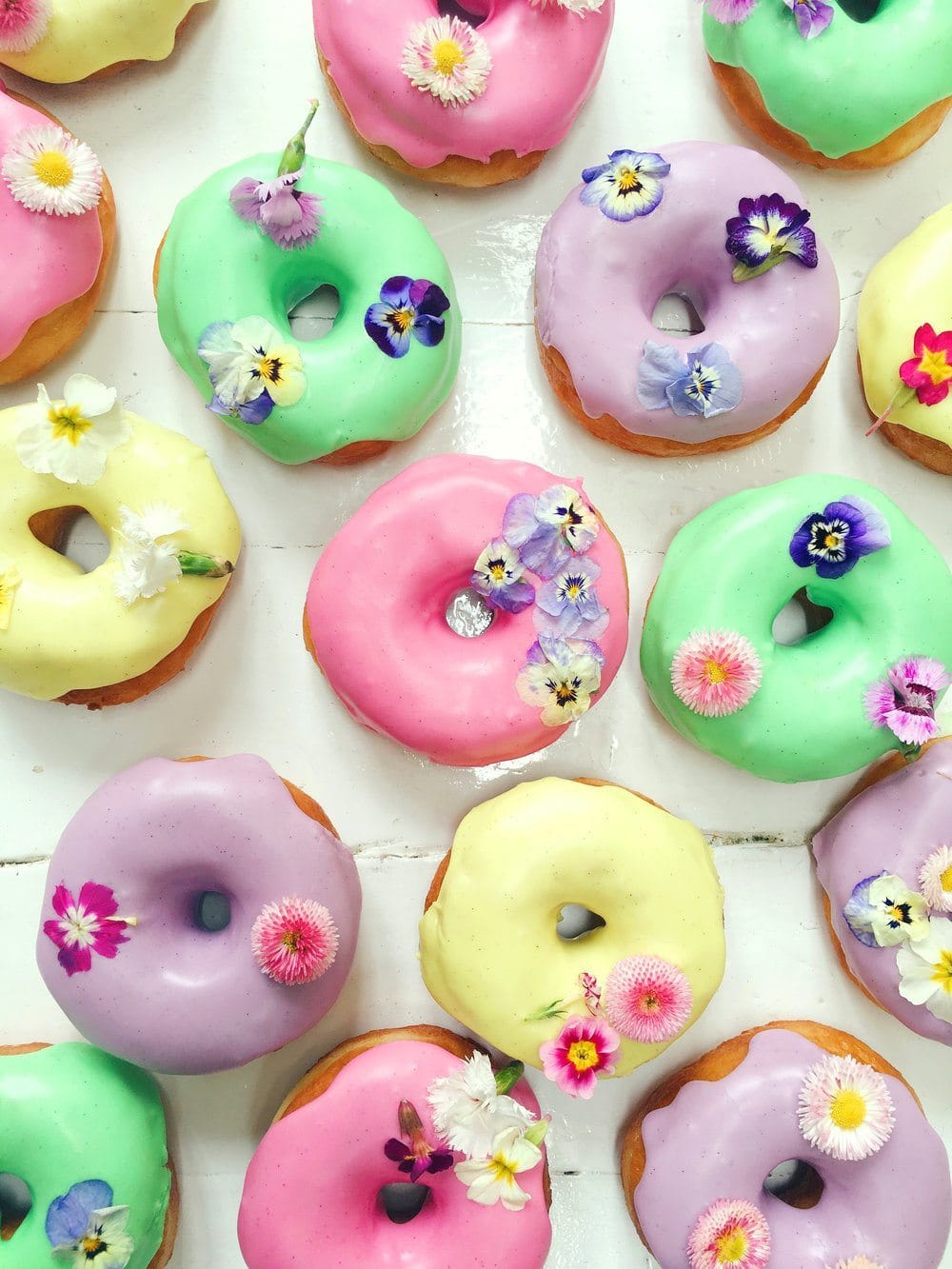 Ring donuts from Vicky's Donuts iced in bright colours and decorated with edible flowers