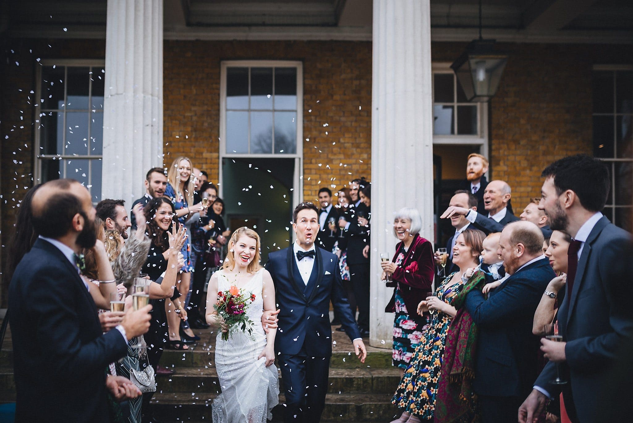 Bride and groom walk through white confetti at Clissold House