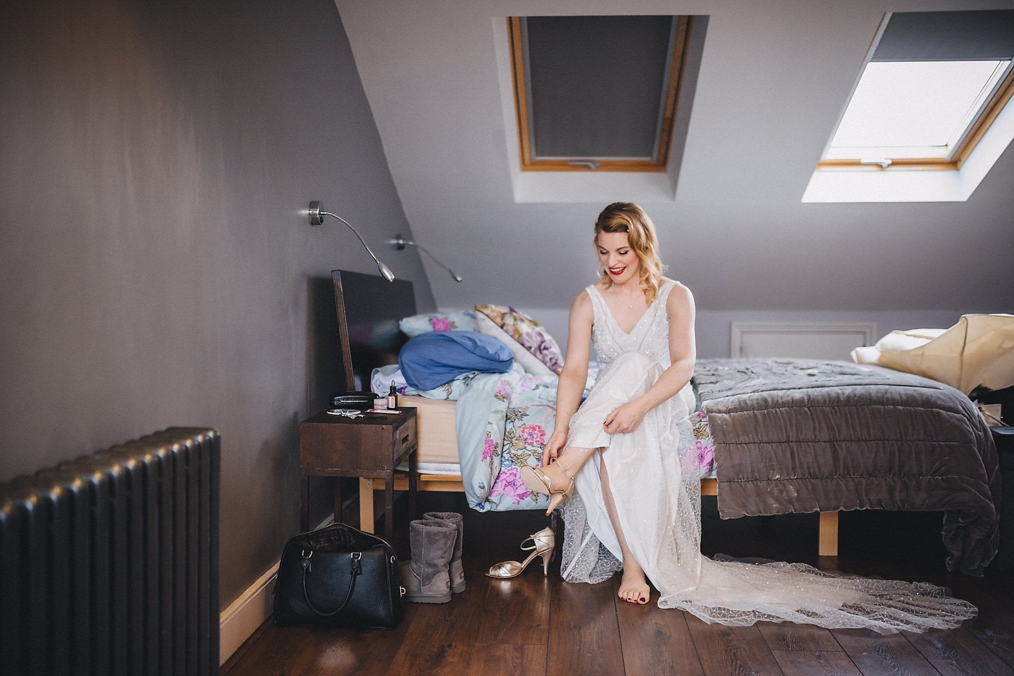 Bride sits on bed and puts her shoes on