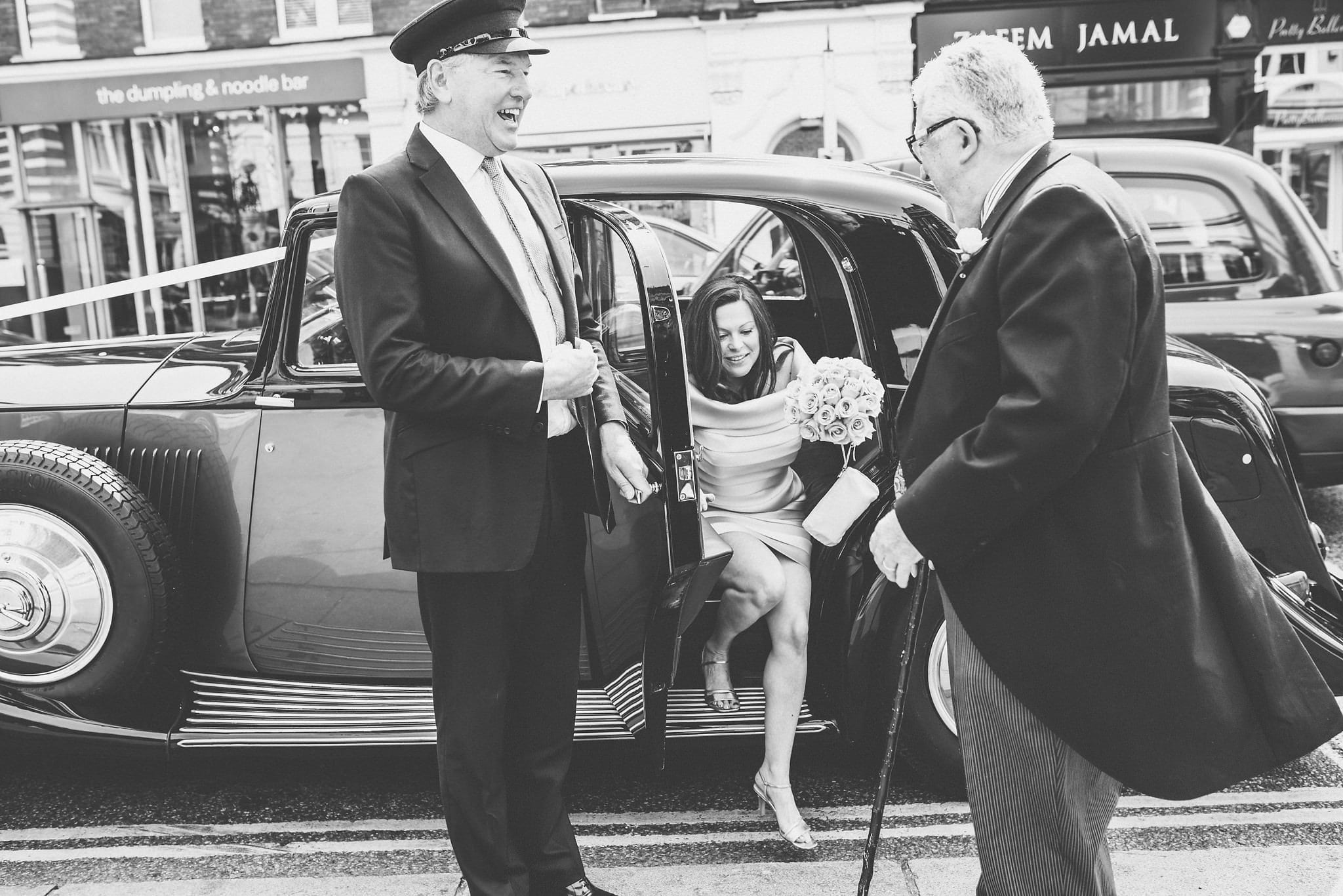 Black and white shot of bride exiting Rolls Royce at her Chelsea Bluebird wedding