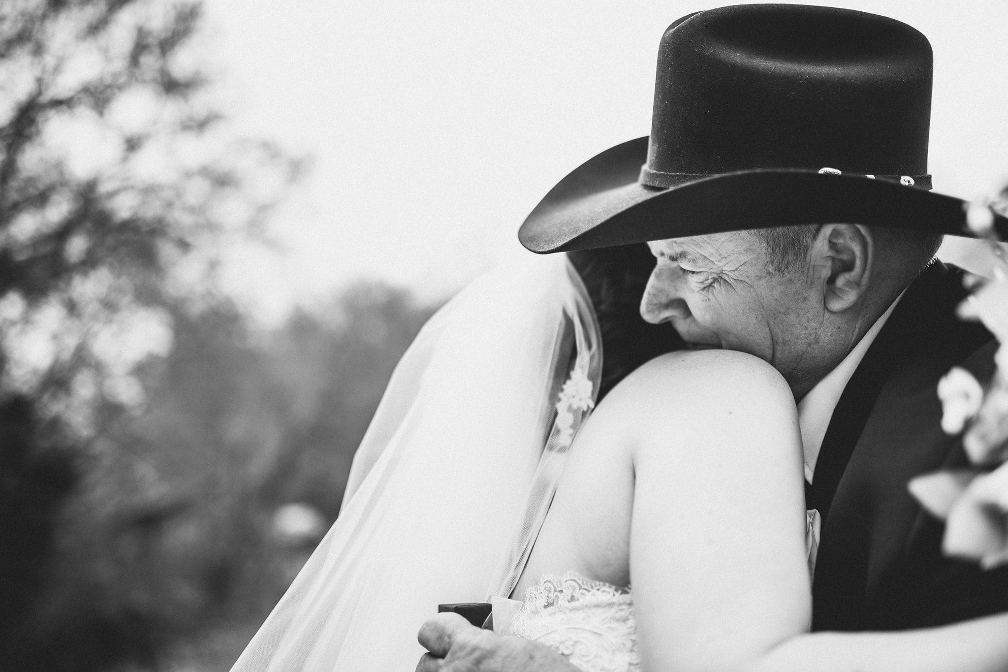 Black and white shot of father of bride in black stetson hugging bride