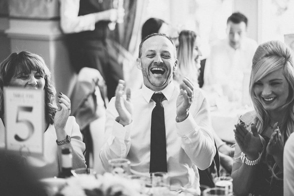 Black and white shot of guests laughing at wedding speech