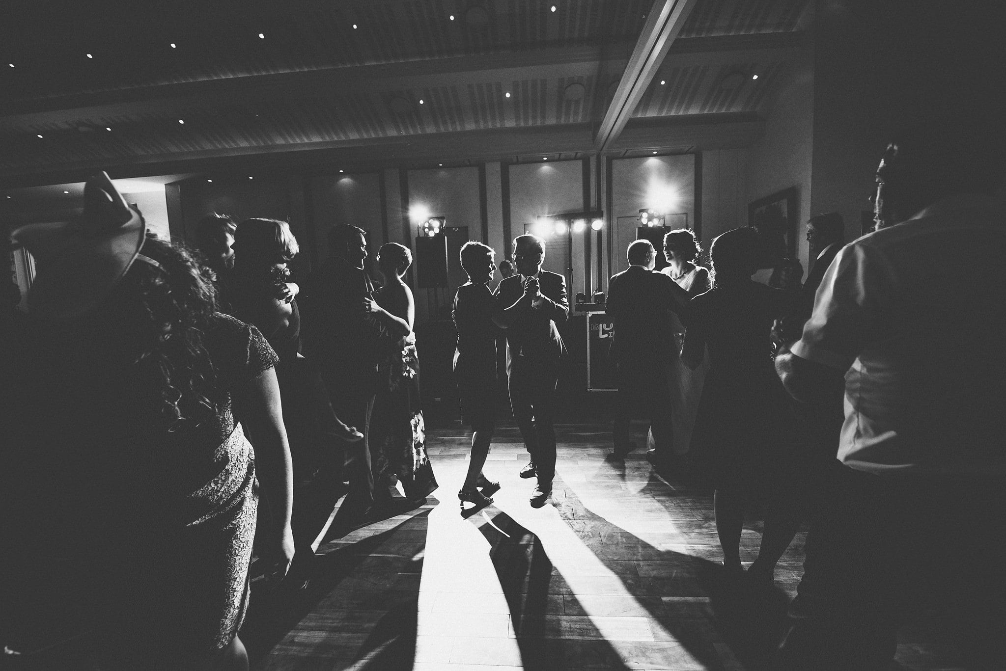 Groom dancing with his mother surrounded by wedding guests in a black and white silhouette