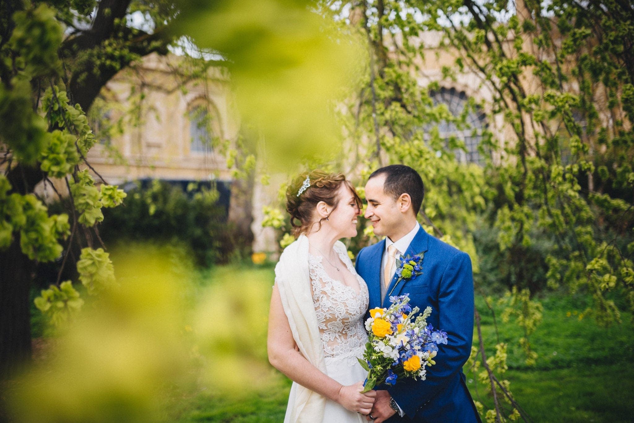 Bride and groom kiss among trees outside Royal Pavilion