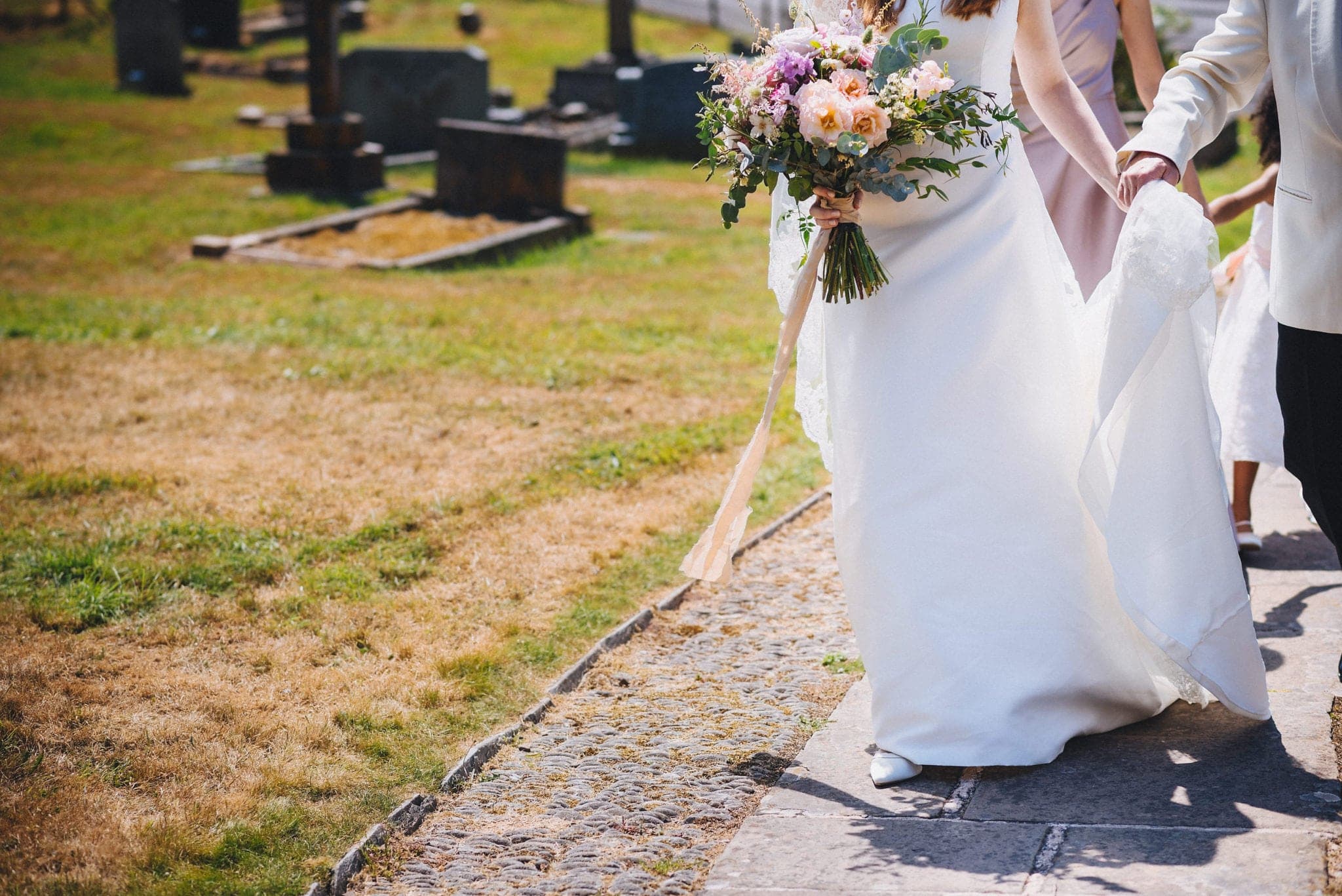 Lower half of bride's dress and bouquet as she walks up path to the church