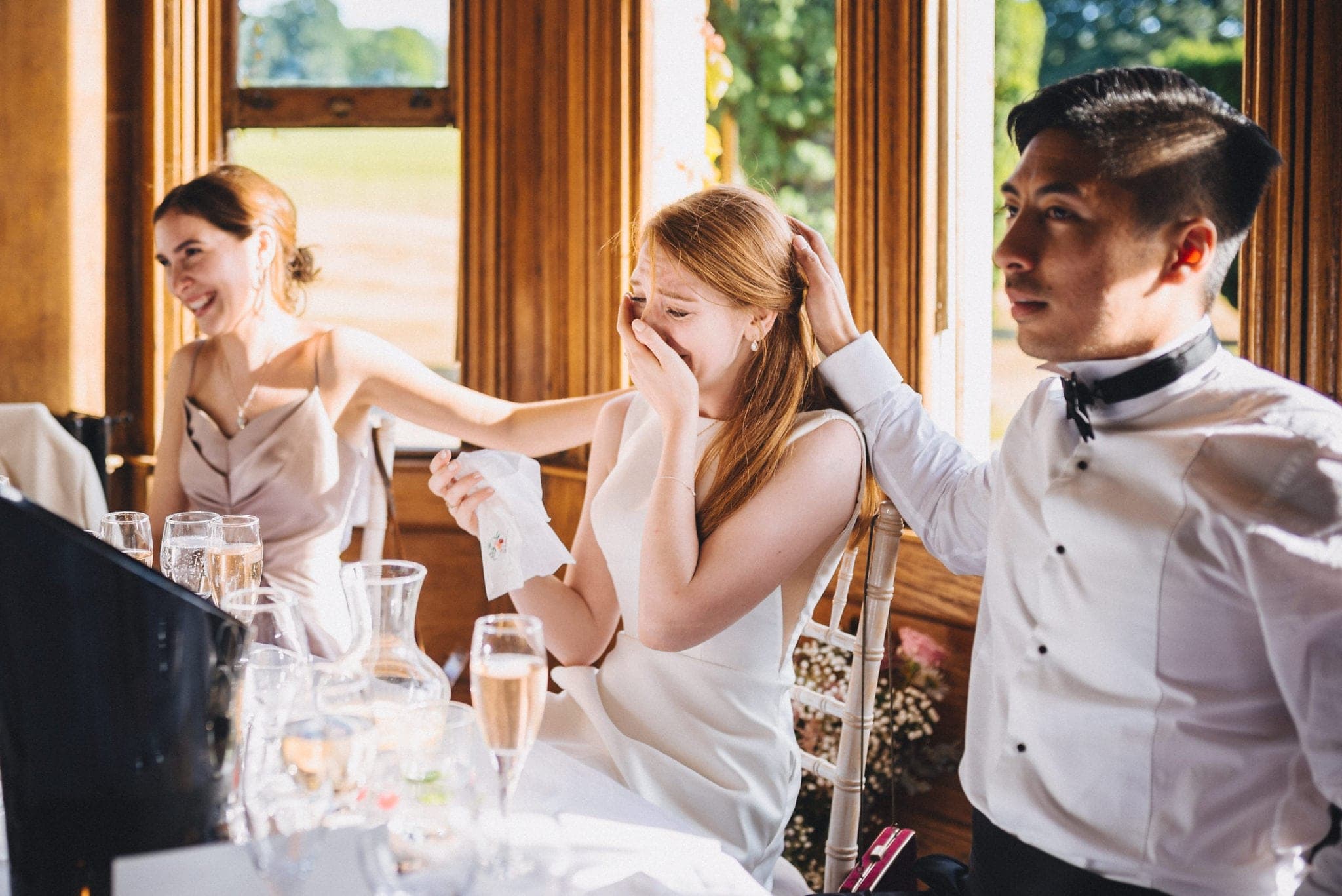 Groom strokes bride's hair as she cries during wedding speeches