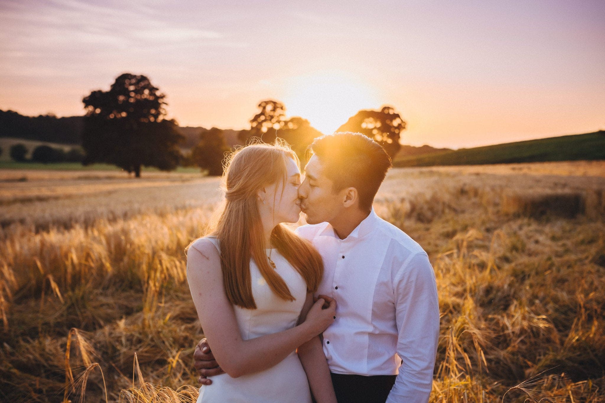 Bride and groom kiss in a wheatfield at golden hour.