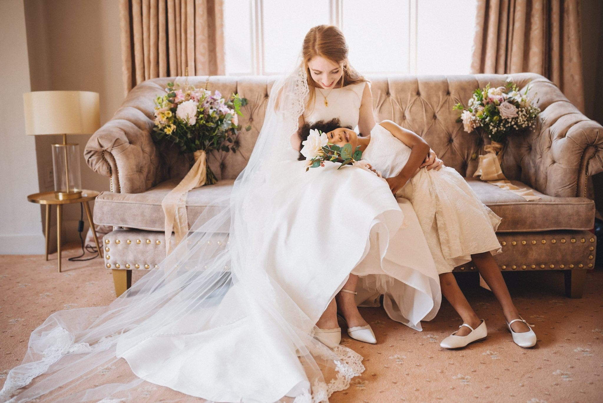 Flower girl lies with her head in bride's lap on velvet sofa