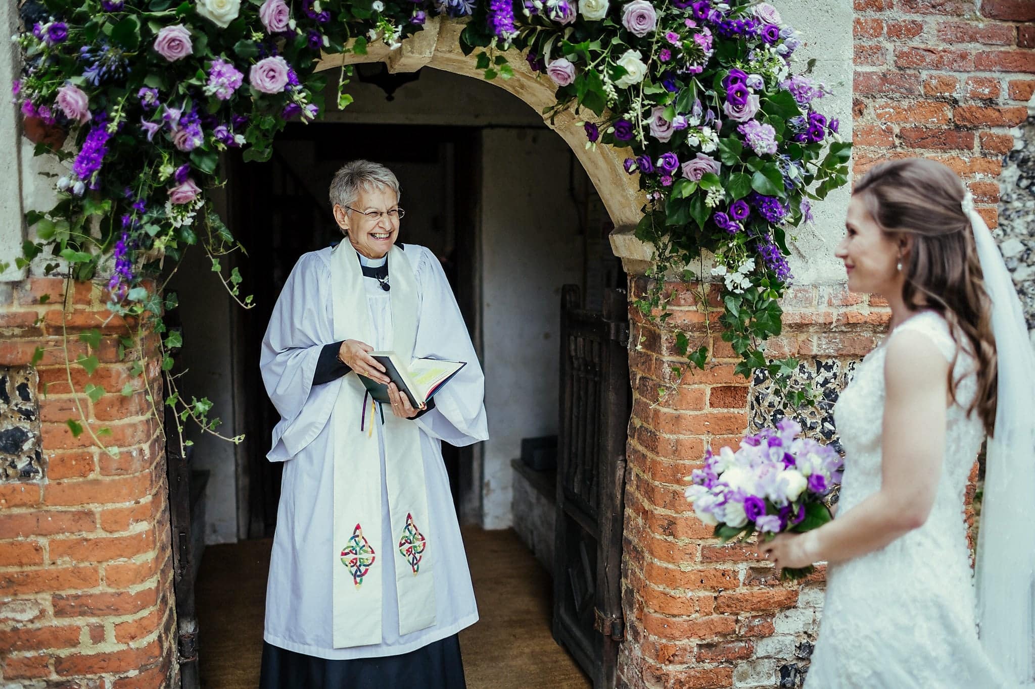 Female vicar greets bride on her arrival at the church at Dorney Court