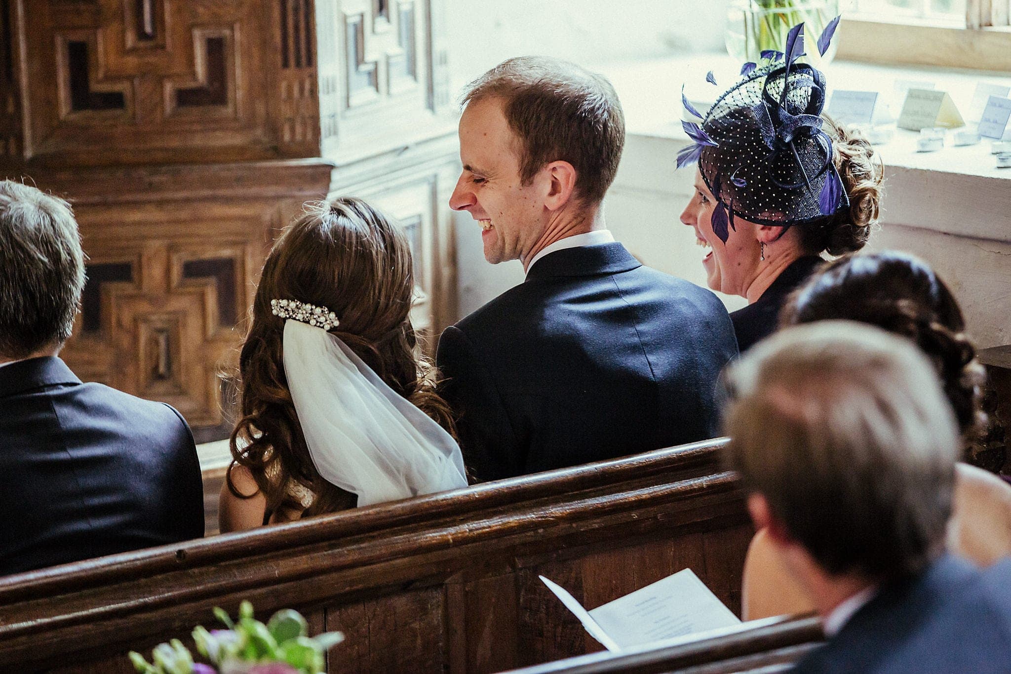 Bride and groom laughing in a pew in church during ceremony