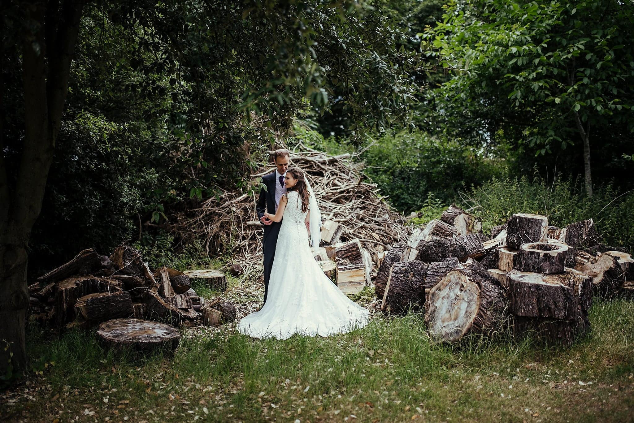 Bride and groom pose amid woodpile in the grounds of Dorney Court