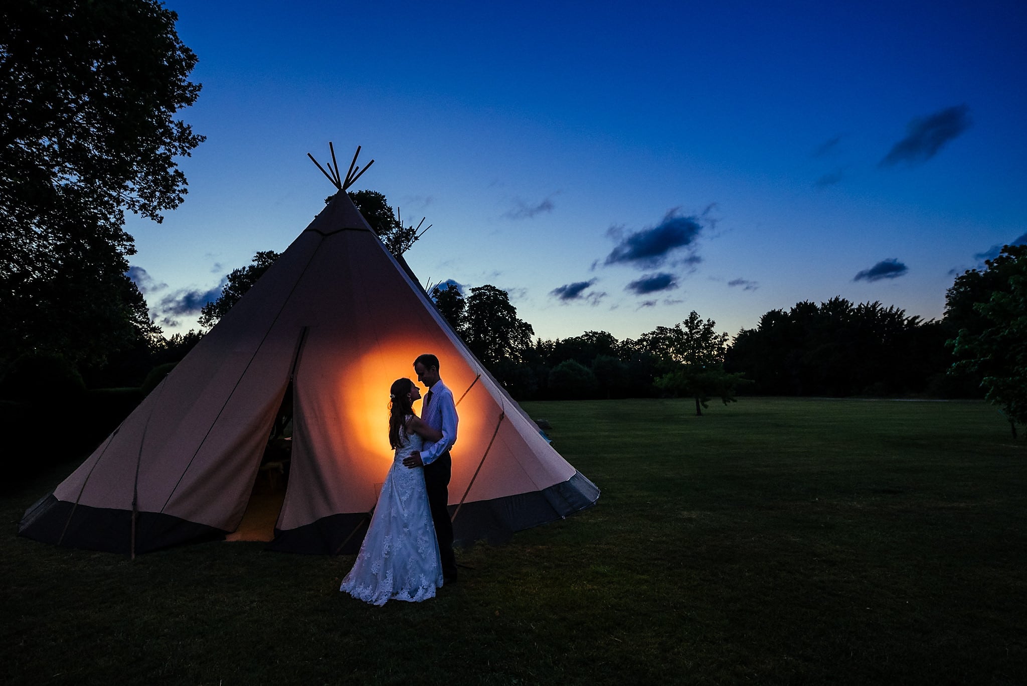 Bride and groom silhouetted in front of tipi in evening light