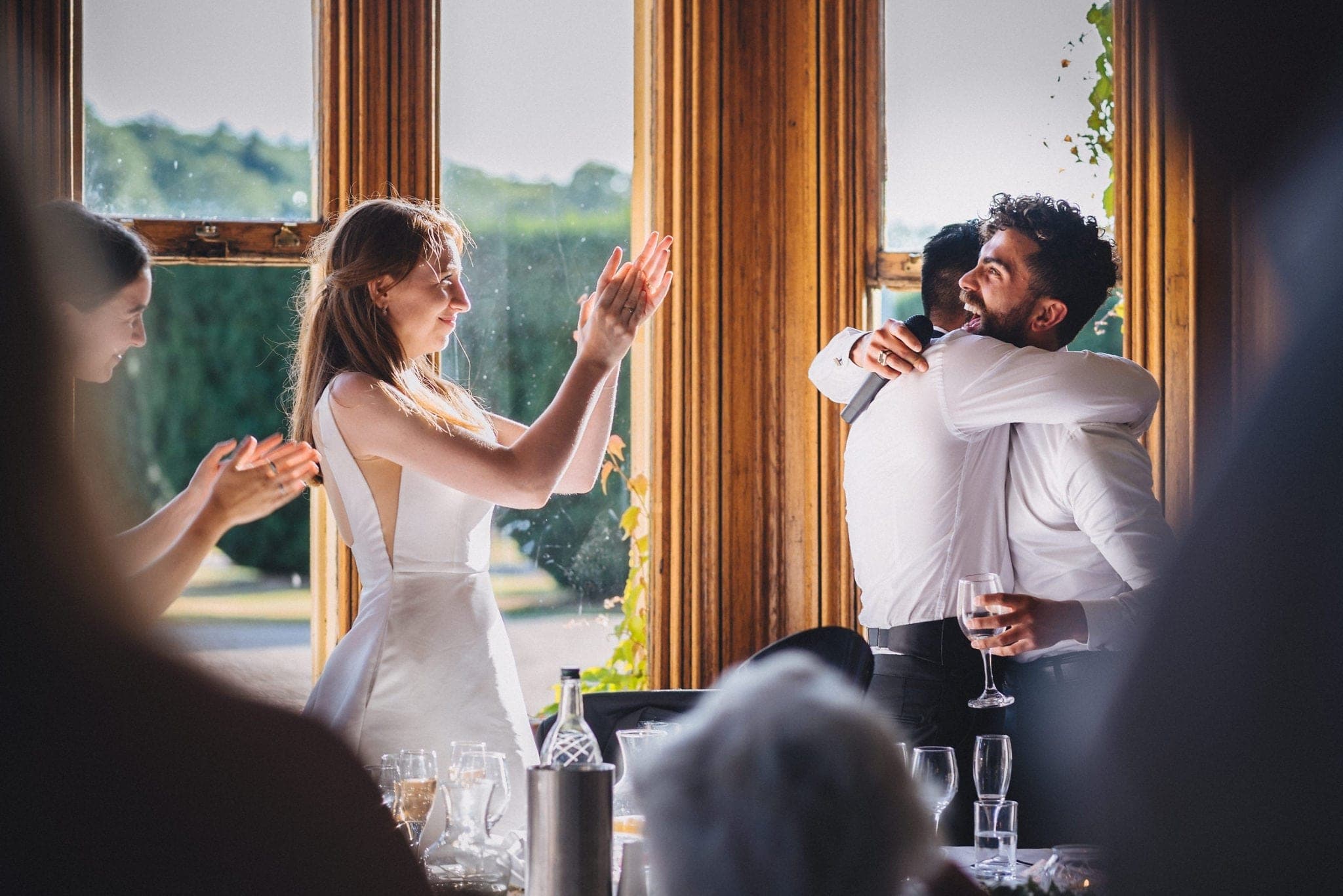 Bride clapping while groom hugs his laughing best man after his speech