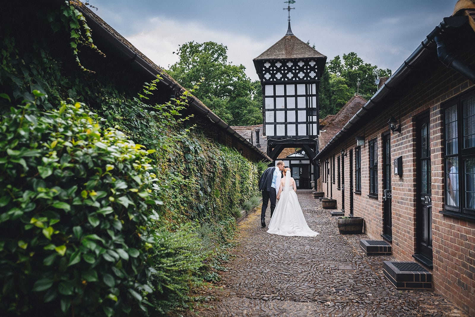 Bride and groom kiss as they walk down towards the main building of the Hever Hotel in Kent