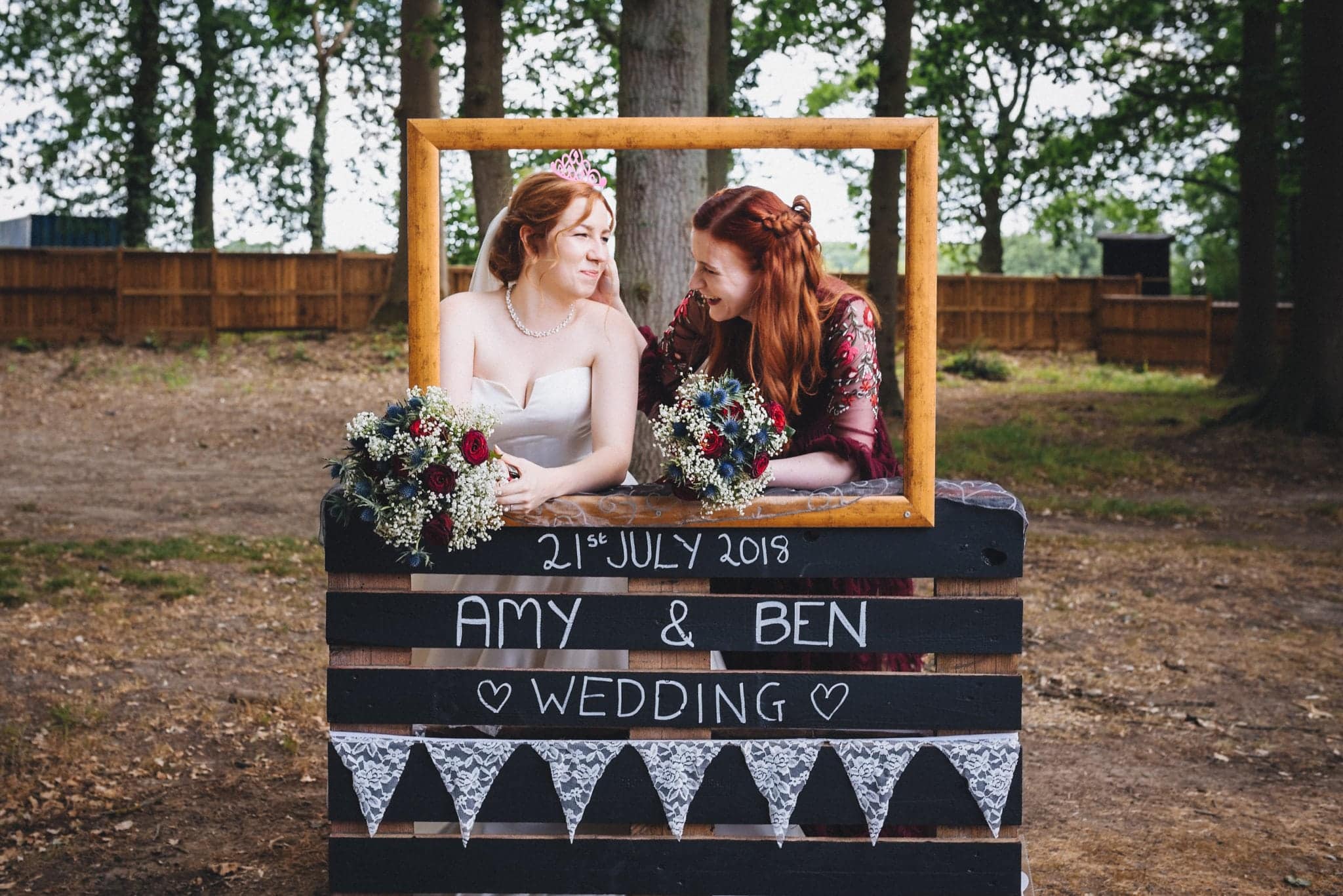 Bride poses with her sister in rustic photobooth in the grounds of Hever Hotel