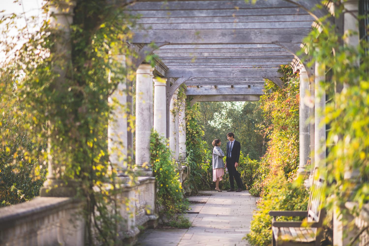 A couple standing surrounded by the luxurious columns of London's Hampstead Pergola