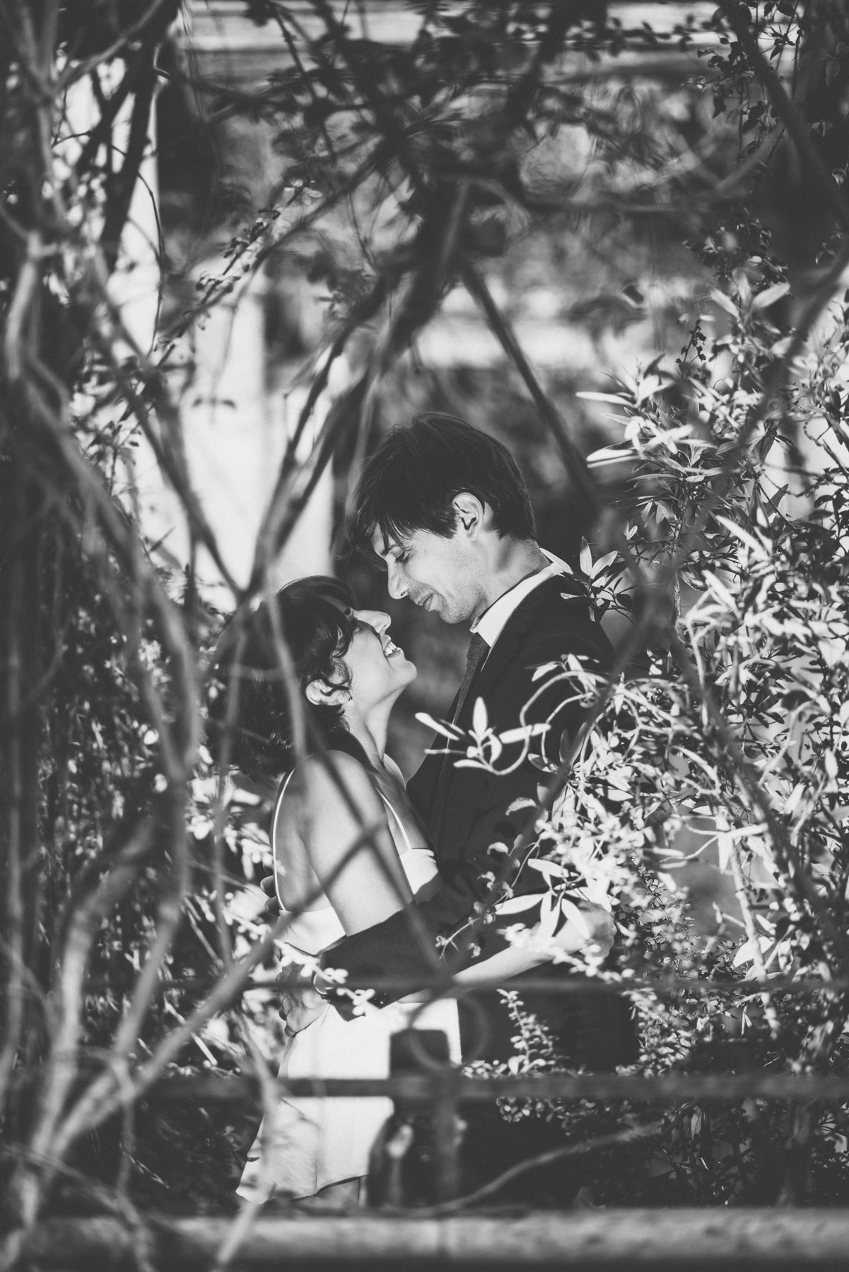 Bride and groom hug before a kiss surrounded by ivy