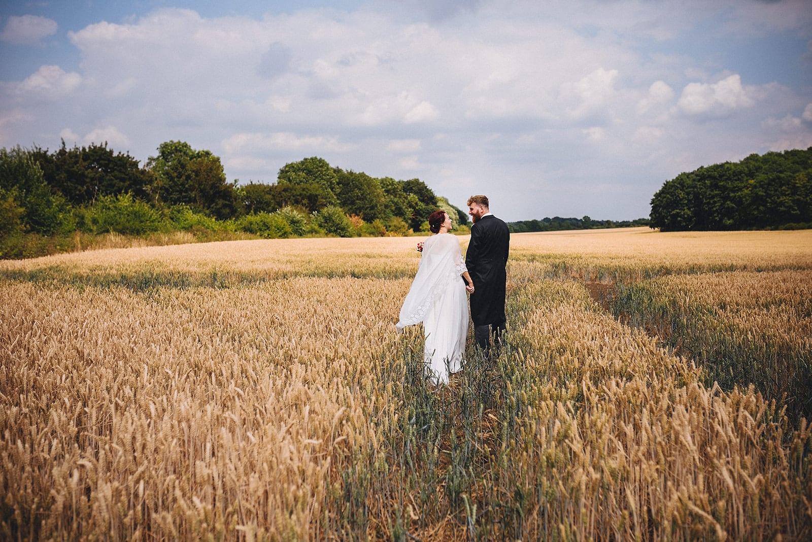 Bride and Groom walking into a corn field at their Joyful Cambridge Farm Wedding