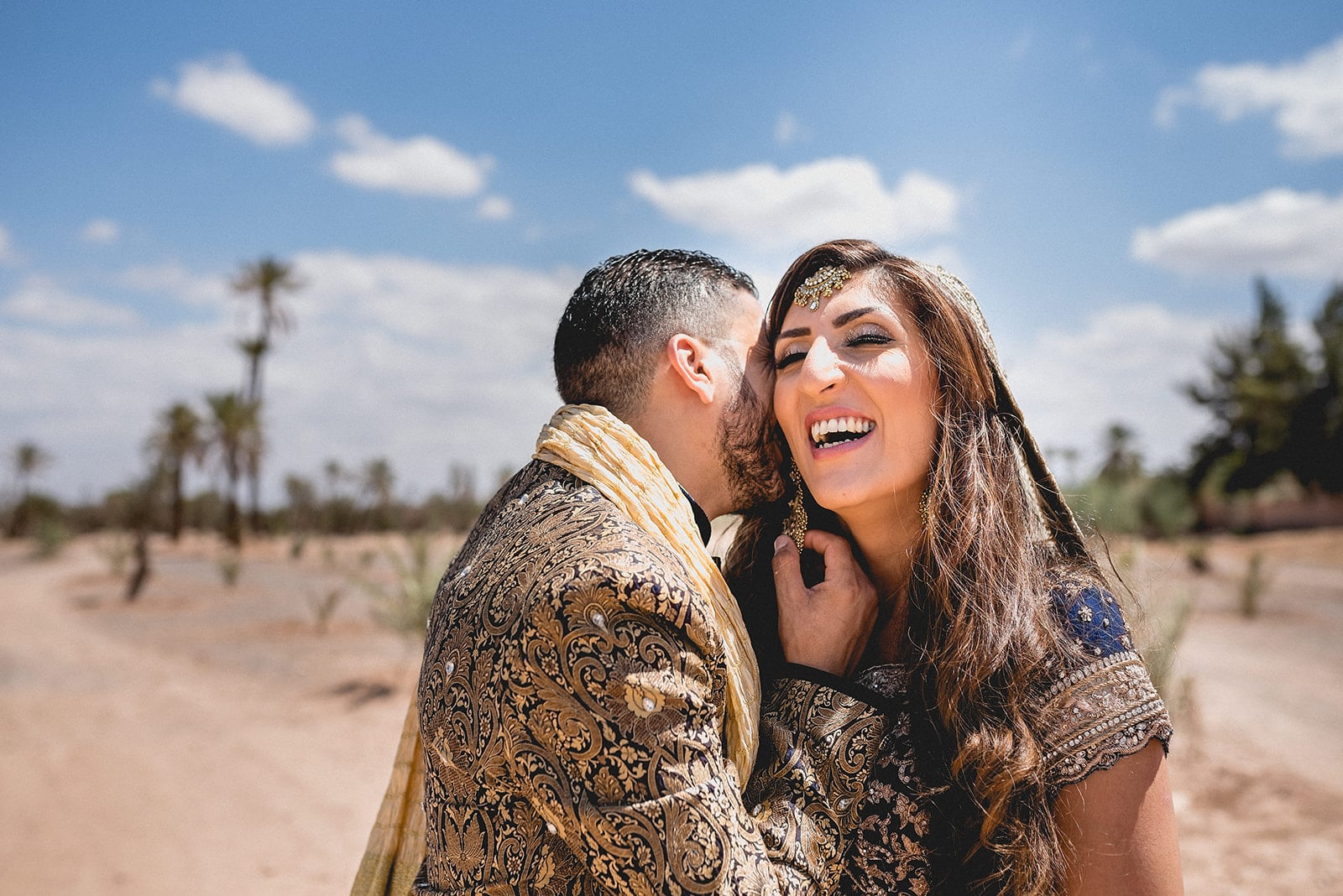 Moroccan Groom whispers into his bride's ear and pulls on her earring while she laughs in the Sahara desert