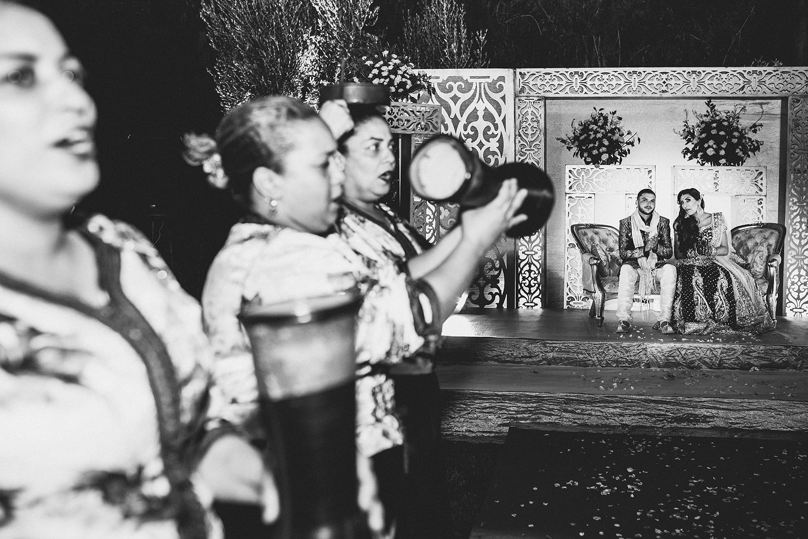 Asian bride and groom sit on the stage while the Moroccan band drums and sings in front of them at their Traditional Moroccan Destination Wedding