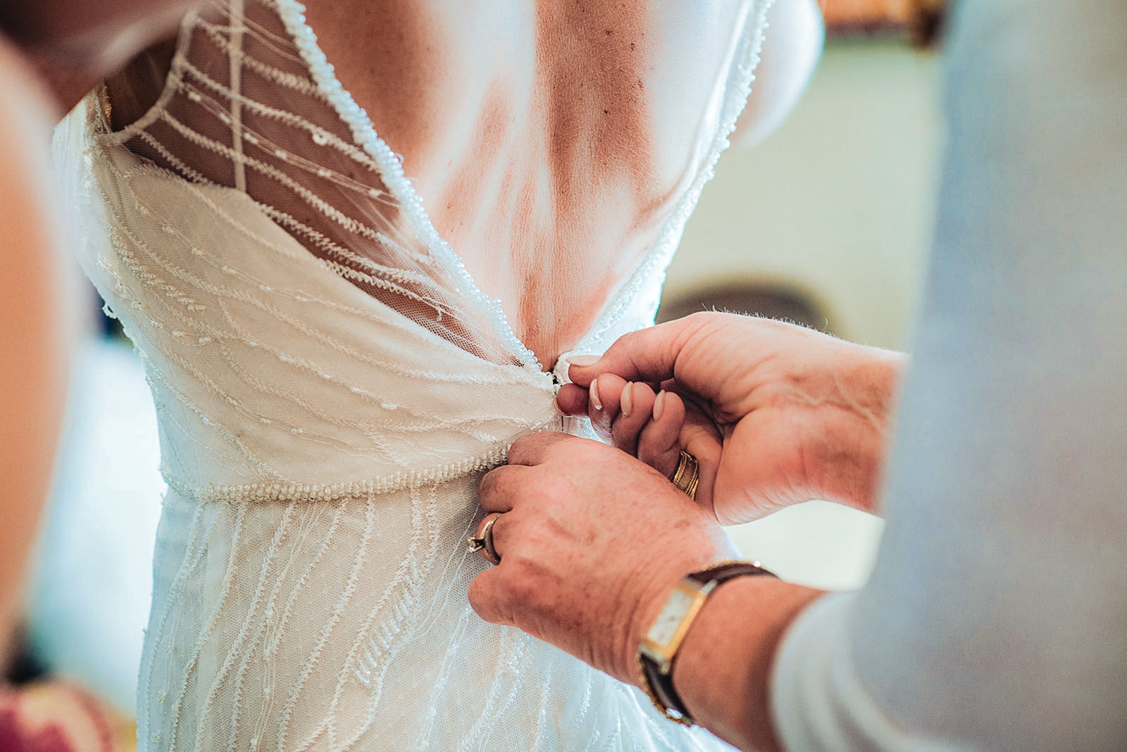 Mum fastening the bride's bead and lace wedding dress