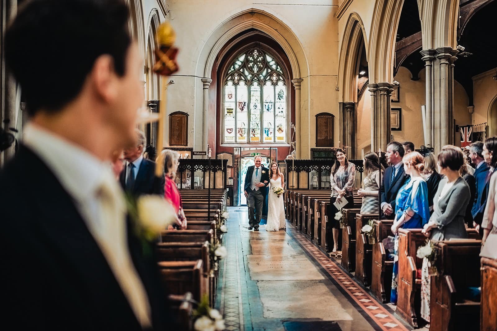 Bride walks down the aisle at All Saints Church in Fulham with her dad smiling at her groom