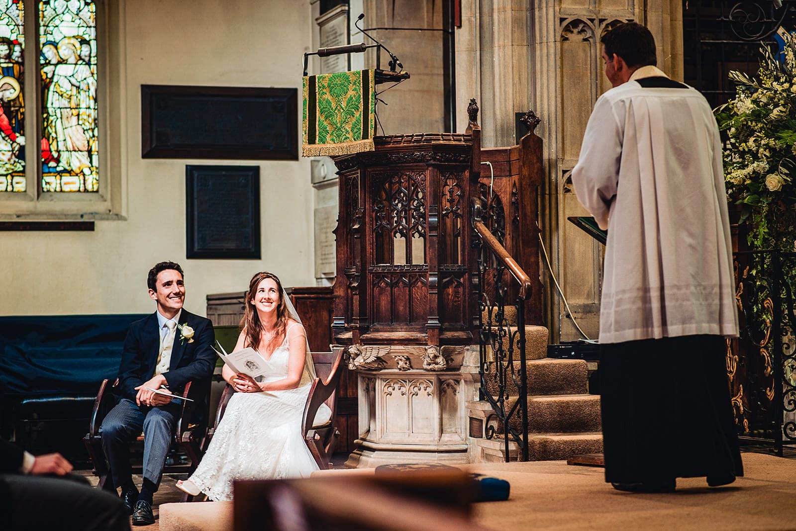 Bride and groom smile as their vicar delivers his wedding sermon