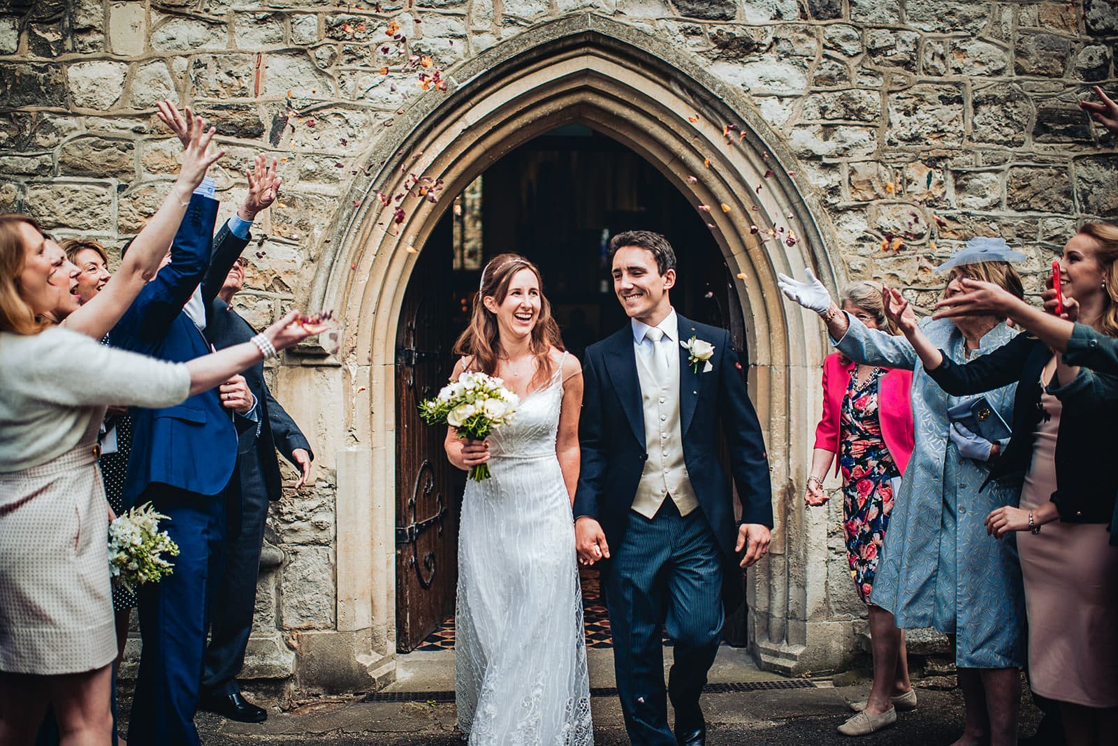 Bride and groom exit All Saints Church in Fulham under rose petal confetti