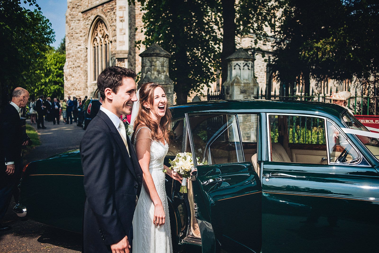 Bride and groom laugh as they get in their vintage wedding car at All Saint's Church, Fulham