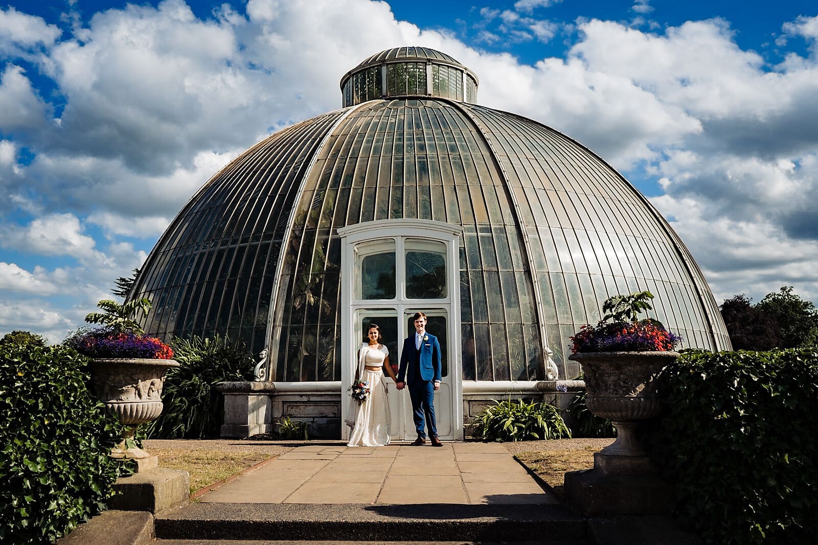 Bride and groom standing in front of the large Palm House at Kew Gardens