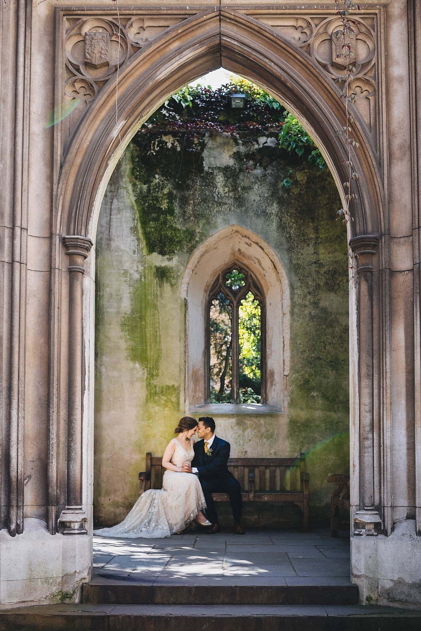 Bride and groom sit close on a bench at St Dunstan in the East in London