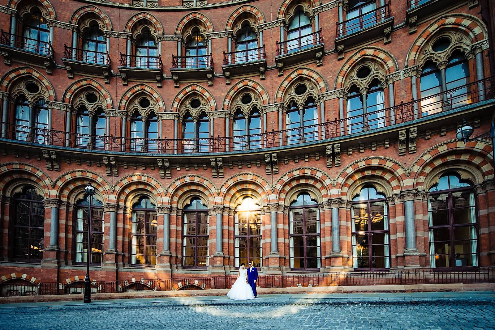 Bride and groom stand in front of the St Pancras Renaissance Hotel surrounded by a sunflare