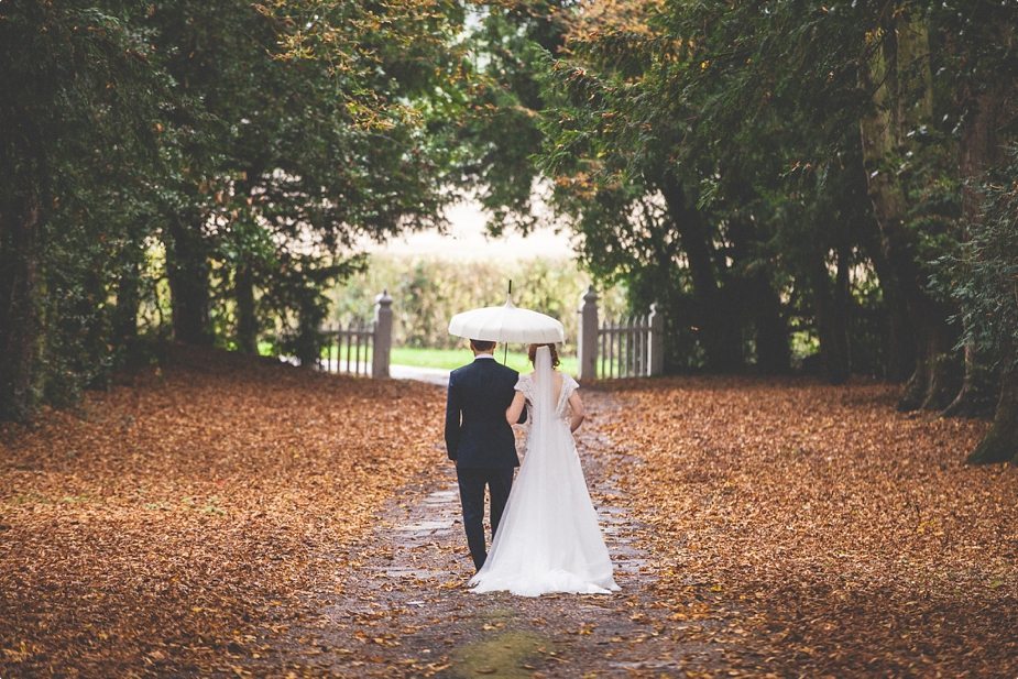 Bride and groom walk through an autumn leaf alley at their Smeetham Hall Barn rustic rainy wedding