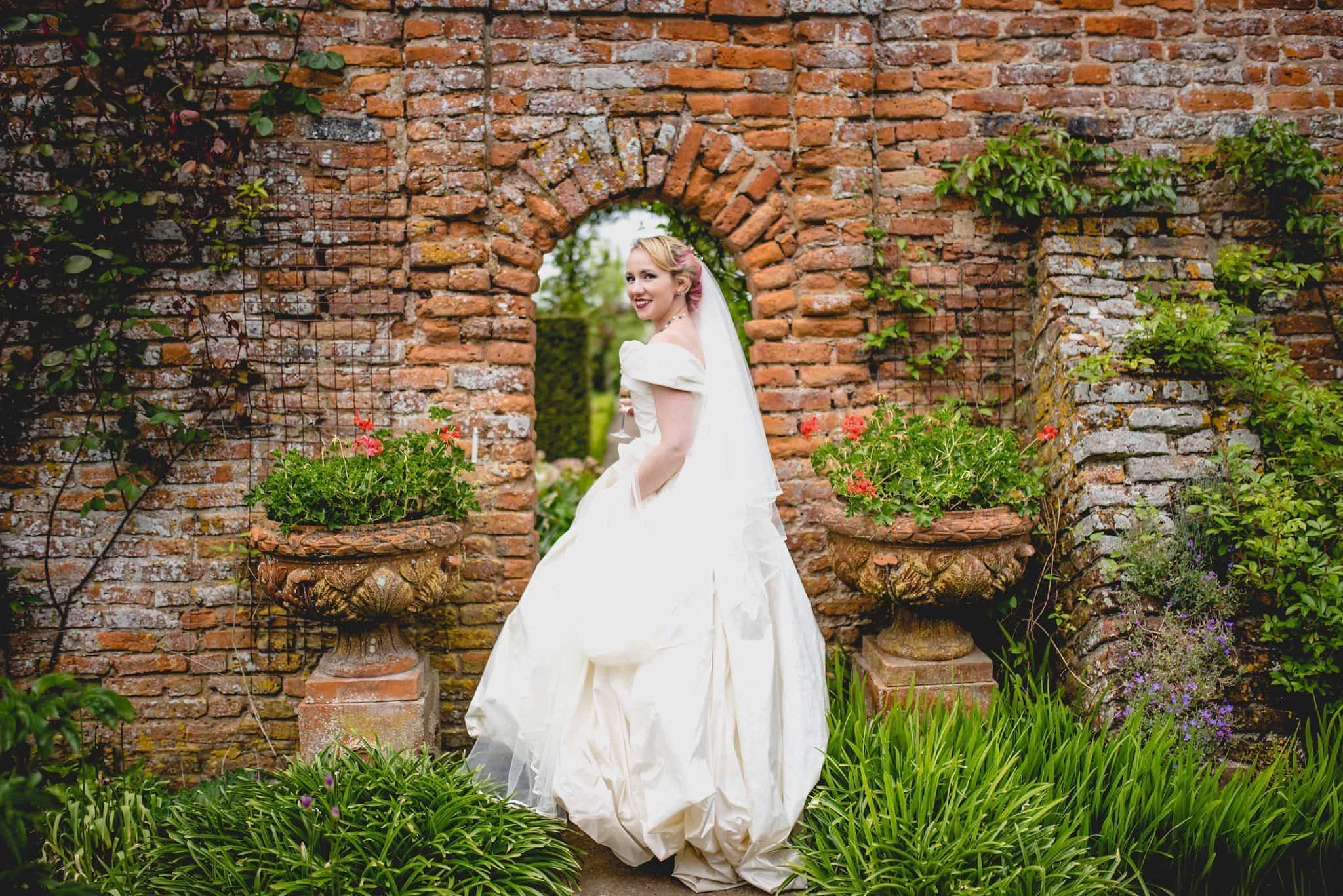 Bride walking through a brick arch at her quirky birtsmorton court wedding