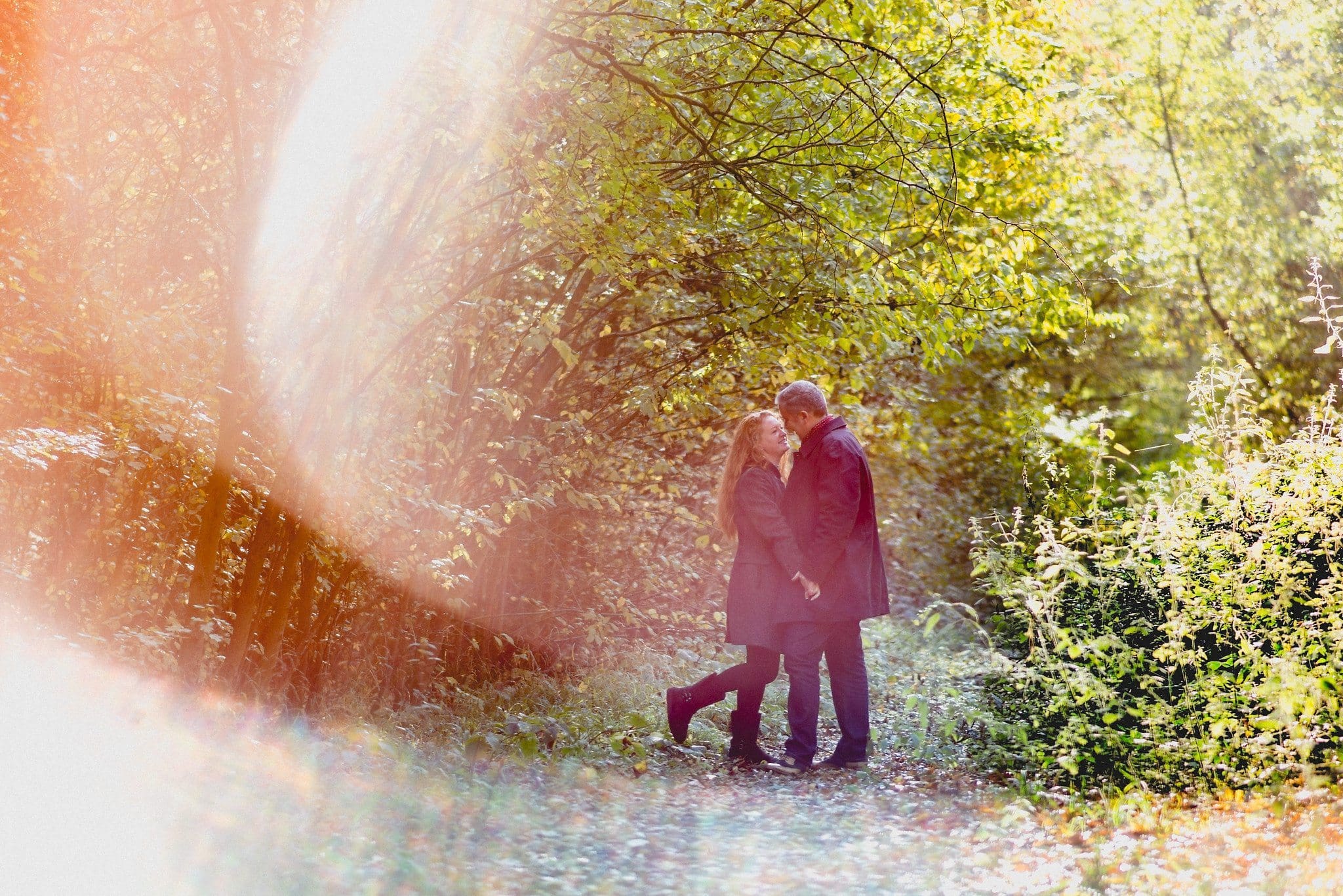 Couple snuggling in the forest framed by a bright sun flare 