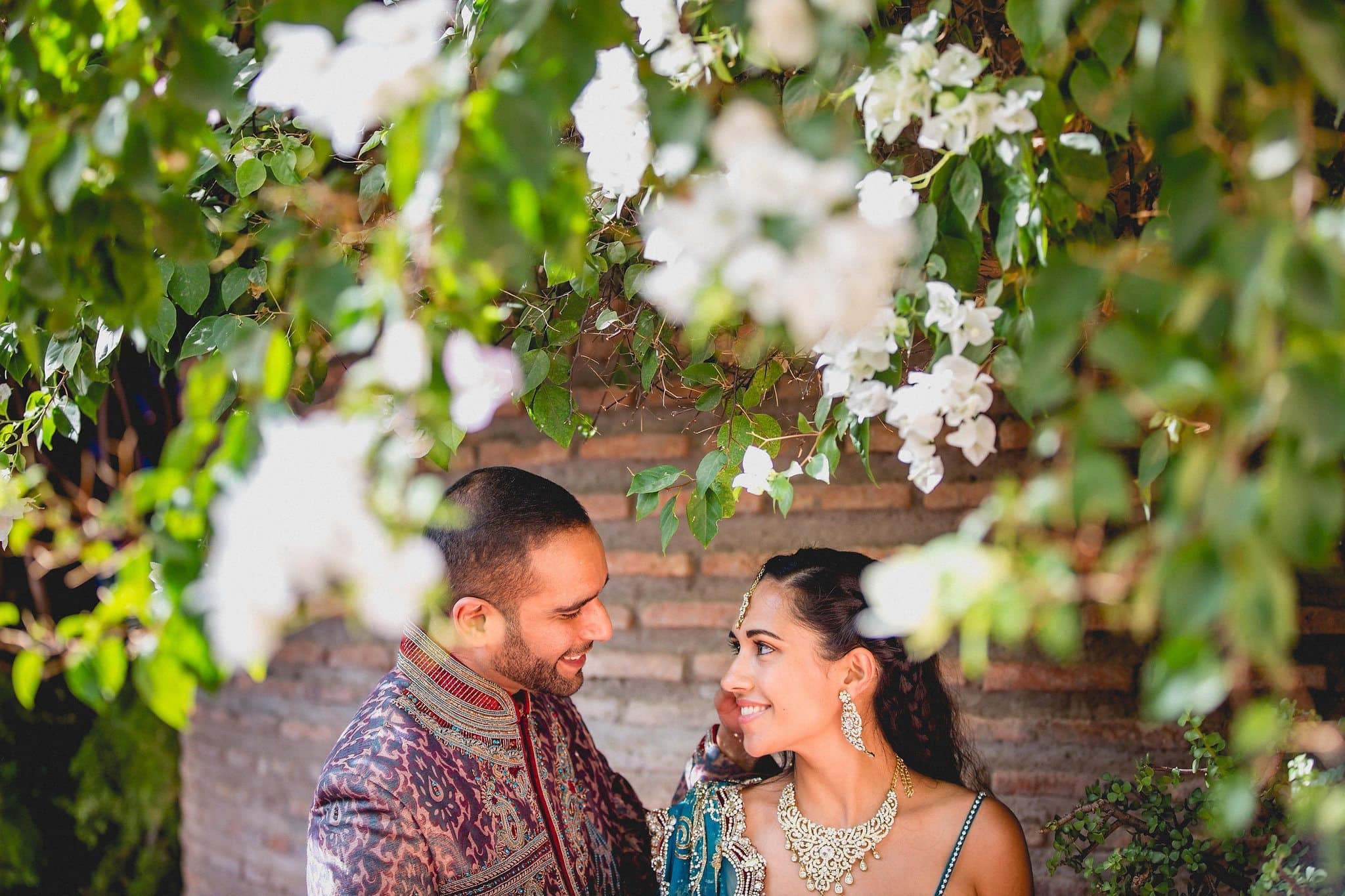 Indian bride and groom gaze at each other under white blooms at the Marrakech Majorelle Gardens