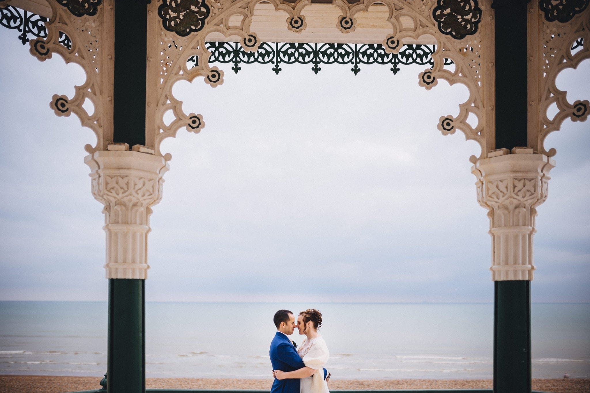 Bride and groom embrace on Brighton bandstand with sea in the background