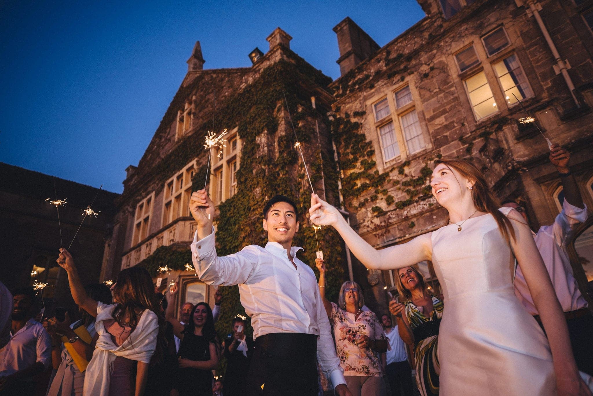 Bride, groom and guests hold sparklers outside manor house at their glamorous St Audries Park wedding