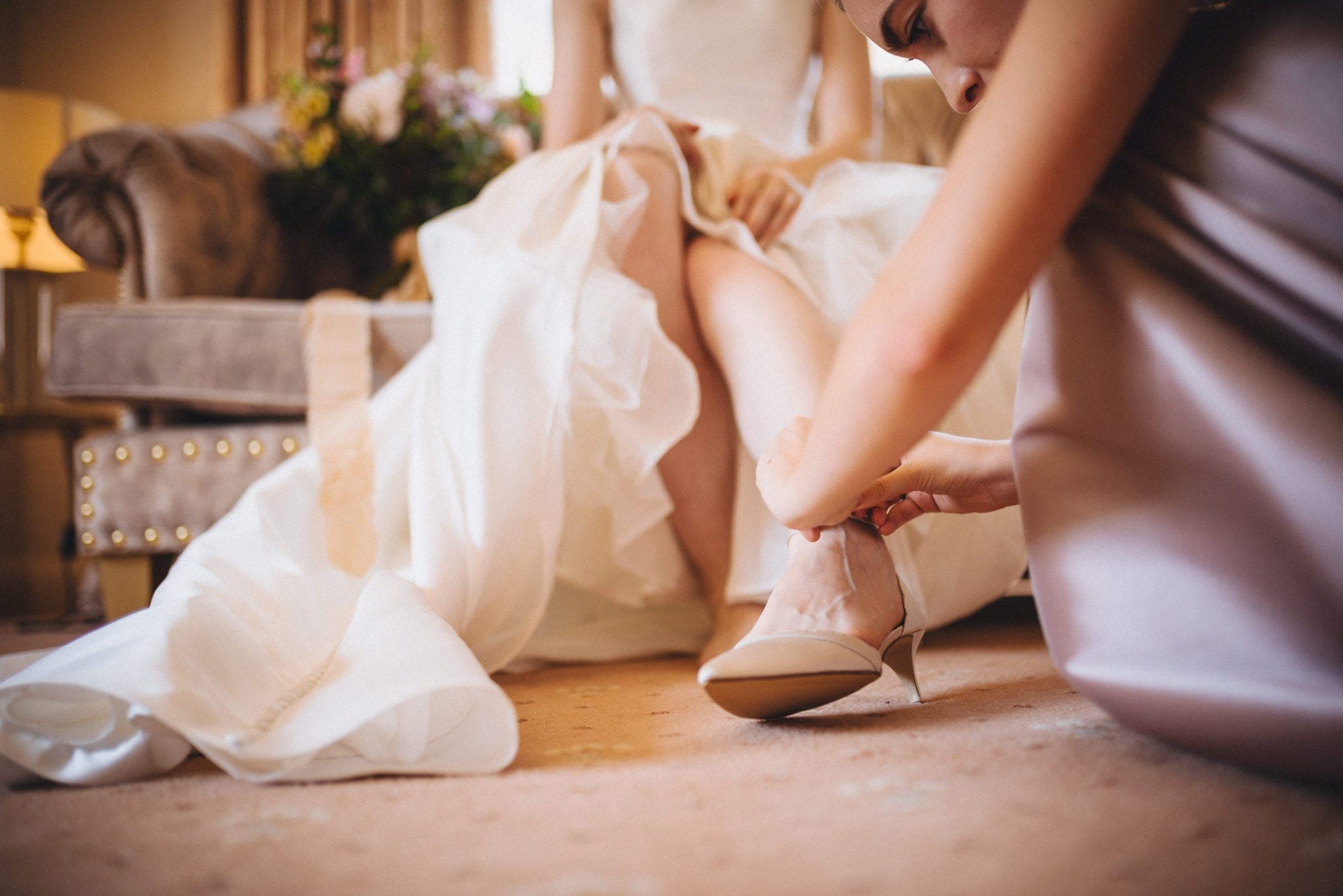 Bridesmaid fastens bride's shoe