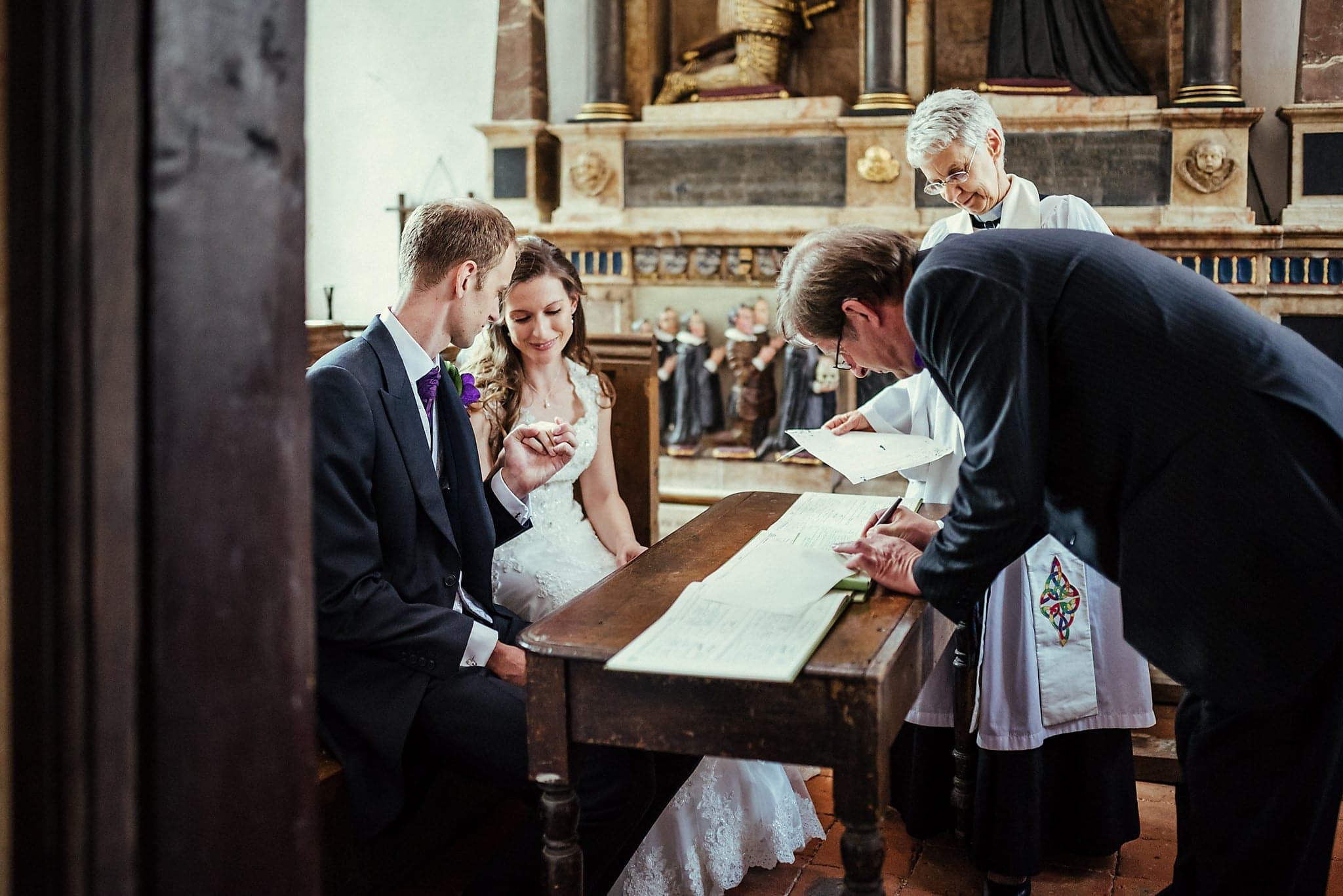 Bride and Groom looking at their rings while the witnesses sign the register at Dorney Court